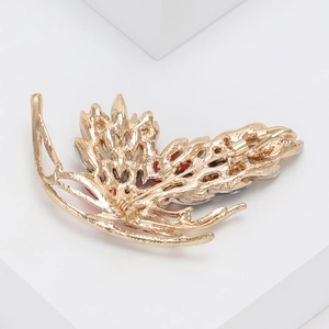 Detail view of gold leaf brooch with hollow design and inlaid crystals on white background