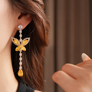 Close-up of model wearing gold butterfly drop earrings with yellow zircon crystals