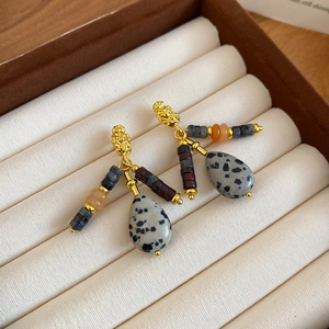 Macro view of gold-plated teardrop earrings with multi-color beads and spotted stones