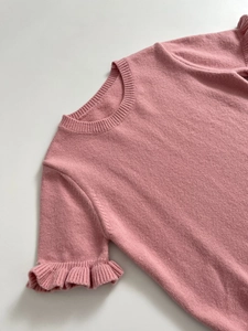 Pink short sleeve knit top with ruffled cuffs and classic round neck on grey background