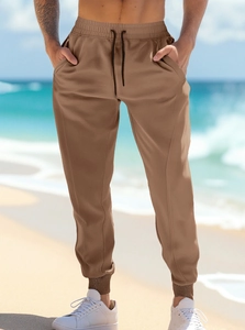 Dettaglio dei joggers marrone caffè con vita elastica e coulisse nera su sfondo di spiaggia