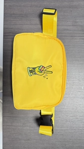 Close-up of a yellow nylon fanny pack featuring a peace sign embroidery on a dark desk