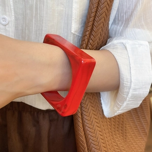 Close-up of a bold red square acrylic bangle paired with casual resort style clothing
