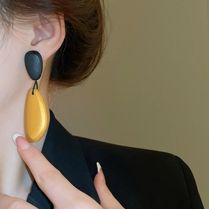 Close-up of minimalist black and yellow oval wooden earrings worn by a female model