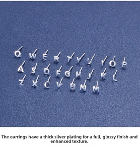 Flat lay view of 26 polished sterling silver letter earrings on a blue textured background