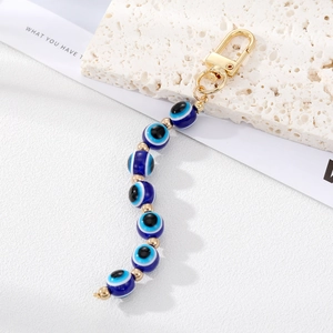 Detail of blue evil eye bead keychain with gold hardware on a textured stone