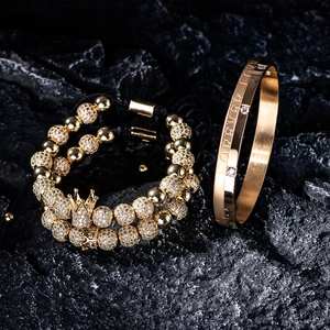 Macro detail of gold Forever Love bracelet set with crown charms on dark stone
