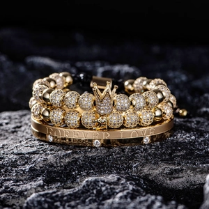 Close-up of gold crown bead bracelets and Forever Love engraved bangle on black rock