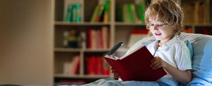 Child reading with a compact black clip-on LED book light on a warm room bookshelf