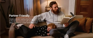 Father reading in bed with soft black clip-on book light while child sleeps peacefully