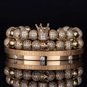 Close-up of golden crown bracelets and Forever Love engraved bangle with zircons