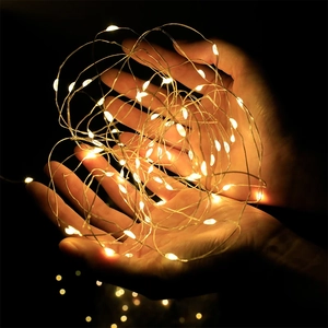 Close-up of warm white LED copper wire fairy lights held in hands over a black background