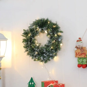 Detail of green artificial Christmas wreath with warm LED lights and faux snow on wood
