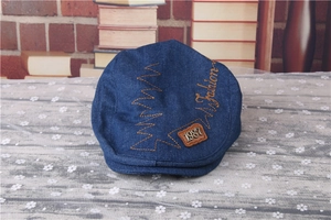 Detail of dark blue denim newsboy cap featuring orange embroidery and fashion text