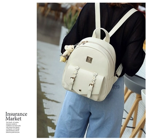 Detail eines cremeweißen PU-Lederrucksacks mit Blumenapplikation und Bärenanhänger