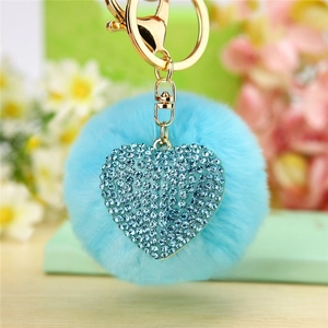 Detail of light blue faux fur pompom and heart pendant with rhinestones on gold keychain