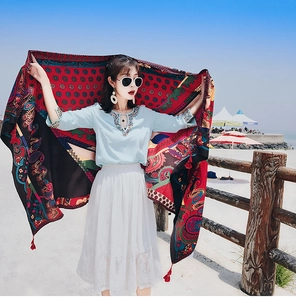 Lightweight bohemian paisley beach shawl with red tassels held against a sunny blue sky