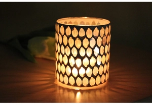 Close-up of glass candle holder with dark metal honeycomb pattern casting warm shadows