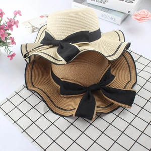 Close-up of woven straw sun hats with black bow ribbon and stylish wavy brim design