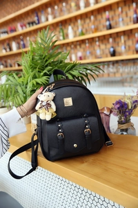 Detail eines schwarzen Lederrucksacks mit goldener Logoplatte und süßem Teddybär-Anhänger