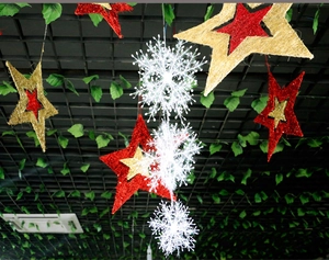 Close-up of sparkling gold stars and white snowflakes hanging on a green leaf background