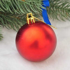 Close-up of matte red Christmas ball ornament with gold cap on green pine needles