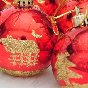 Close-up of red mirror Christmas ball with gold glitter reindeer and tree patterns