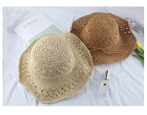 Detail of woven straw hats with scalloped edges and bow ribbons on a linen surface