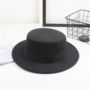 Detail shot of a black wool felt flat top hat with ribbon on a decorative white desk
