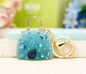 Detail of green handbag keychain with blue gemstones and elegant gold-tone hardware