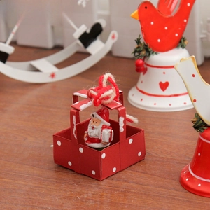 Close-up of a festive red metal gift box ornament with a small Santa Claus inside