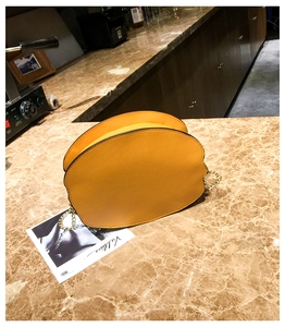 Detail of creative bright yellow crossbody bag with gold chain on marble surface