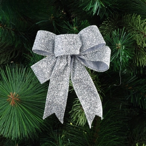 Detail of a sparkling silver sequined Christmas bow ornament hanging on a pine tree
