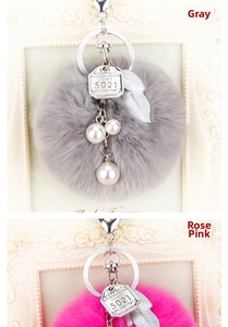 Détail du porte-clés en peluche avec pompons gris et rose, perles et plumes en métal