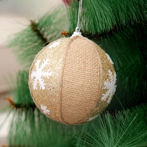 Close-up of rustic burlap Christmas ball with white snowflakes on green tree needles