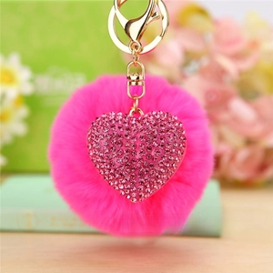 Macro detail of pink pompom keychain with a rhinestone heart charm and golden metal clasp