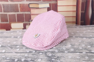 Detail view of red and white striped kids flat cap with shield emblem on lace fabric