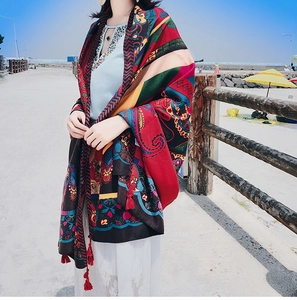 Detail of bohemian shawl with multicolor ethnic print and red fringe tassels by the sea