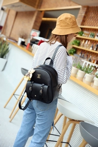 Schwarzer PU-Lederrucksack mit Goldbeschlägen und Bärenanhänger, von Model im Café getragen