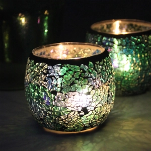 Close-up of mosaic glass candle holders with green and blue textures and warm candle light