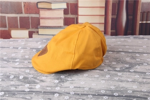 Side view of a bright yellow kid's beret cap with a brown leather patch on retro background