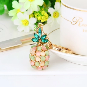 Exquisite pineapple keychain with cat eye stones on a white tray with elegant floral decor