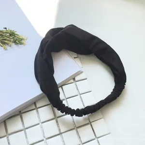 Detail of a black knitted twist headband with elastic back on white tiled background