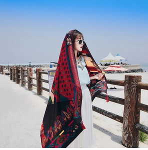 Detail of bohemian red paisley print beach shawl on model against blue sky