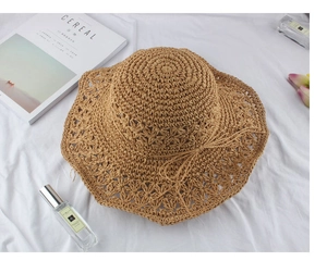 Detail of tan woven straw sun hat with delicate hollow floral pattern and wide brim