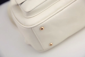 Detailaufnahme der weißen PU-Ledertasche mit goldenen Metallfüßen und feinen Nähten am Boden