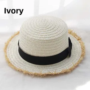 Detail of cream-white boater hat with a black bow ribbon and frayed straw edges