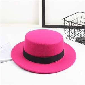 Detail of rose red felt flat top boater hat with a black grosgrain ribbon on white surface