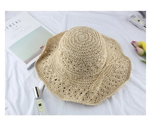 Close-up of oatmeal straw hat with wavy brim and bow on white fabric background