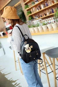 Detail eines schwarzen PU-Lederrucksacks mit goldenen Reißverschlüssen und Teddy-Anhänger